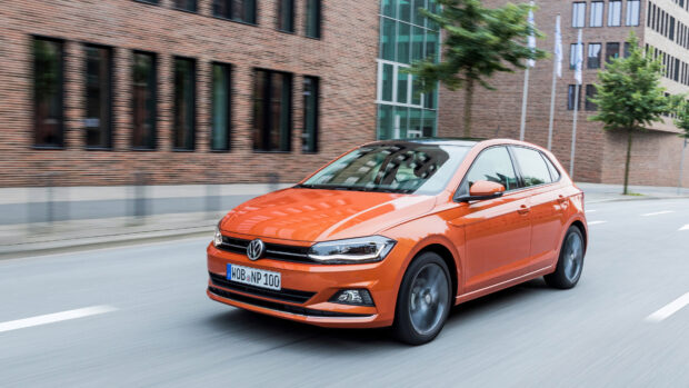 Orange Volkswagen car driving on city street with modern buildings
