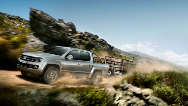 Volkswagen Amarok truck driving fast on a dirt road in a mountainous area