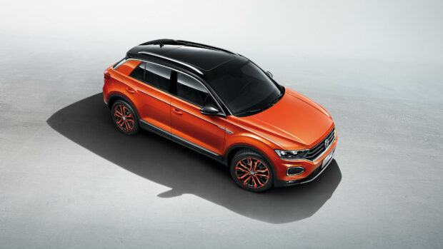 A vibrant orange Volkswagen SUV parked on a concrete surface casting a long shadow