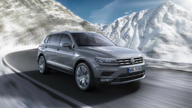 A Volkswagen SUV driving on a mountain road surrounded by snow covered peaks