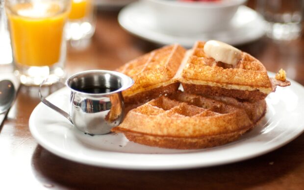 A stack of golden waffle with butter and syrup on a white plate on wooden table
