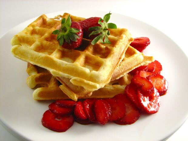 Golden waffle with strawberries served on a white plate showing fresh strawberries and waffle squares