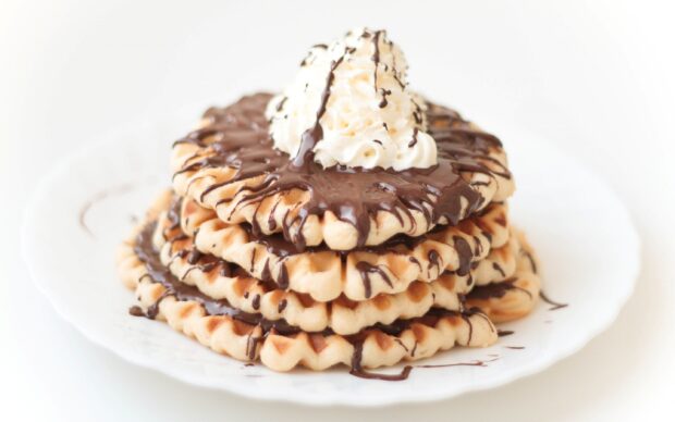 A stack of waffle topped with whipped cream and drizzled chocolate on a white plate