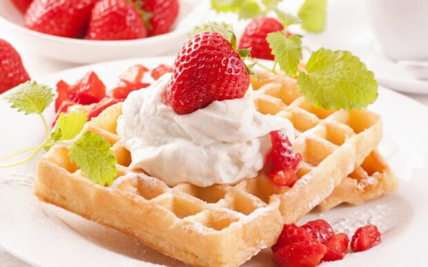 Crispy waffle topped with whipped cream and fresh strawberry as waffle decoration