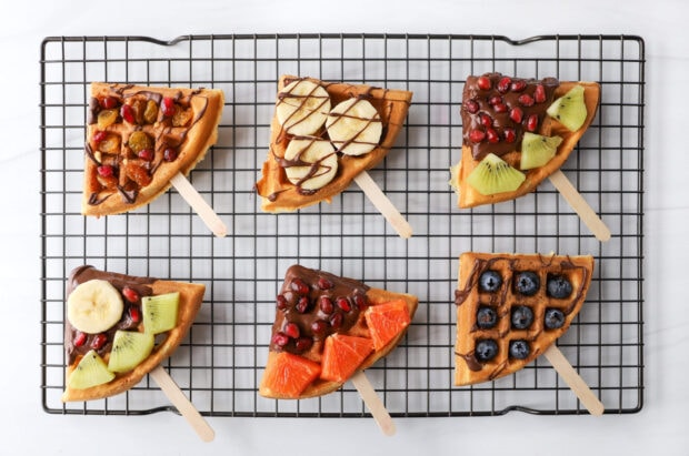 Delicious waffle slices topped with various fruits and chocolate on a cooling rack