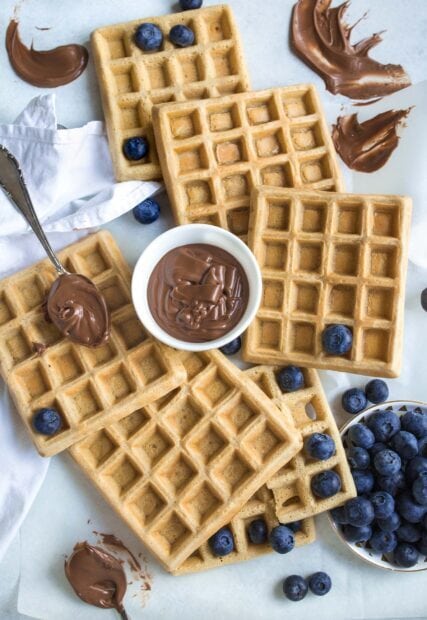 Delicious waffle topped with fresh blueberries and creamy chocolate spread on a white surface
