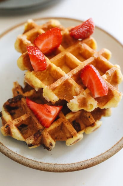 Fresh waffle topped with sliced strawberries on a ceramic plate