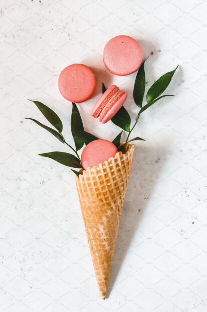 Pink macaron flowers with green leaves in a waffle cone on white marble