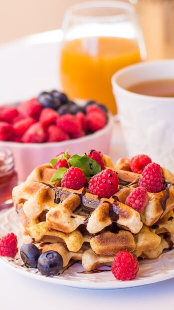 A stack of waffle topped with raspberries and fresh mint leaves