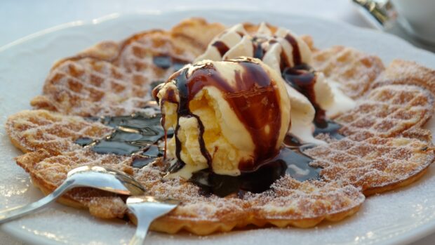 A delicious waffle topped with vanilla ice cream and chocolate syrup on a white plate