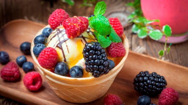 A waffle cup filled with ice cream garnished with fresh berries and mint leaves