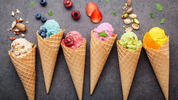 Colorful ice cream scoops in waffle cones with nuts and fruits on a dark surface