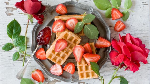 Delicious waffle topped with fresh strawberries and green leaves on a vintage plate