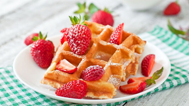 A close up of waffle topped with fresh strawberries and powdered sugar on a plate