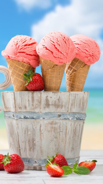 Strawberry ice cream scoops in waffle cones with fresh strawberries and mint leaves on a rustic bucket