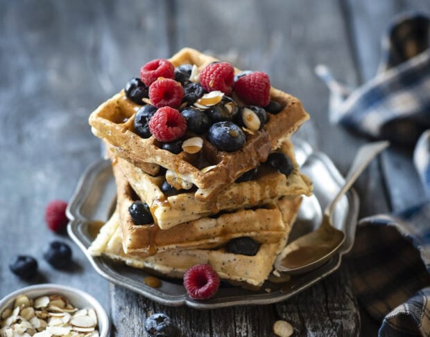 A stack of waffle topped with fresh raspberry blueberry and almond slices