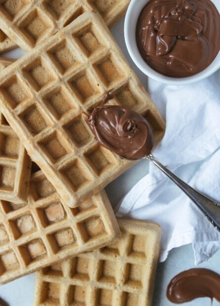 Delicious waffles with smooth chocolate spread on a spoon close to stacked waffles