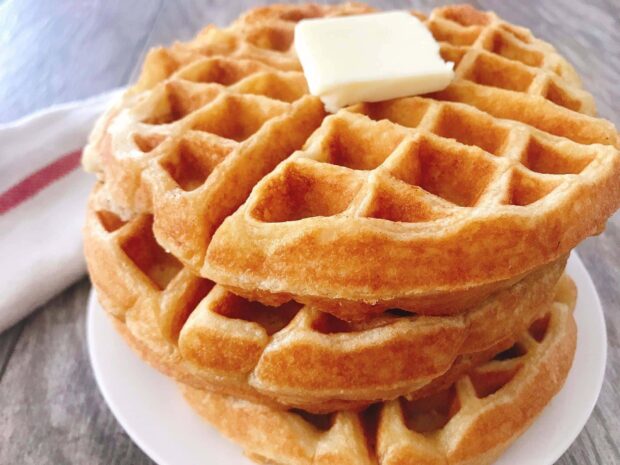 Freshly baked waffle topped with a square of butter on a white plate
