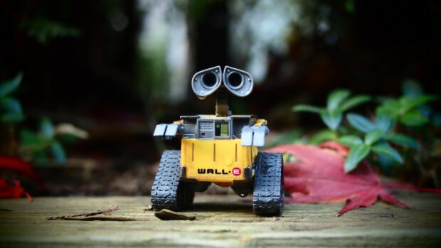 Wall E robot toy standing on wooden surface with autumn leaves around it
