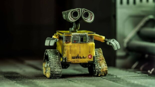 A small yellow robot figure with tank treads standing on a metallic surface in a dark environment