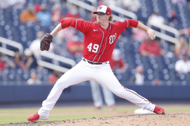 A Washington Nationals player pitching the ball in a baseball game wearing a red jersey and white pants