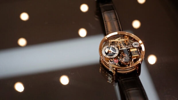 A detailed mechanical watch with a black leather strap placed on a reflective surface with round light reflections