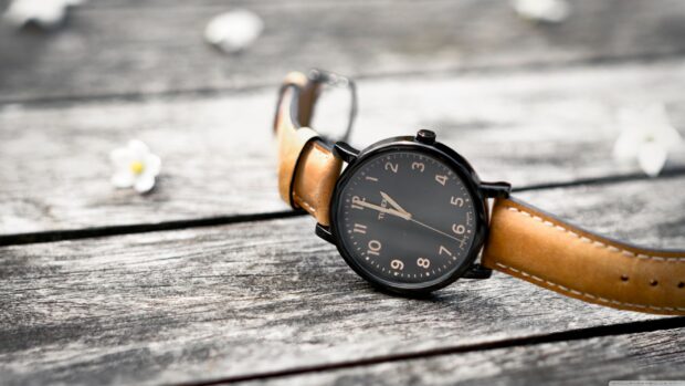 A classic watch with a brown leather strap resting on a wooden surface showcasing the detail of the watch face
