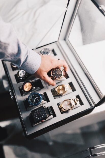 A person selecting a watch from a collection of luxury watches in a display box