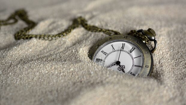 Antique watch partially buried in sand with Roman numerals on the dial