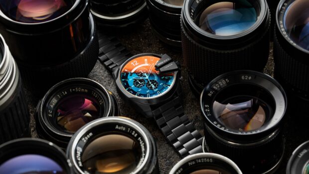A black wristwatch with a colorful dial surrounded by camera lenses on a dark surface