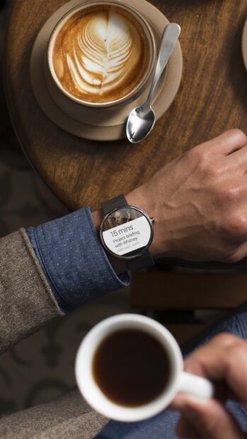 A smart watch displaying a project briefing notification on a wrist near a cup of coffee