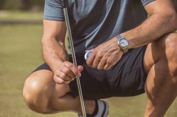 Man wearing a stainless steel watch while holding a golf ball and club on the field