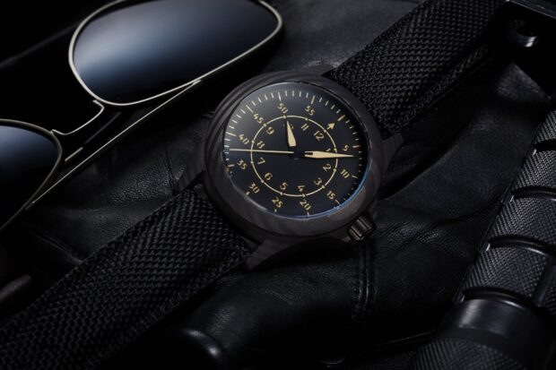 Black watch with fabric strap and detailed dial placed on leather surface