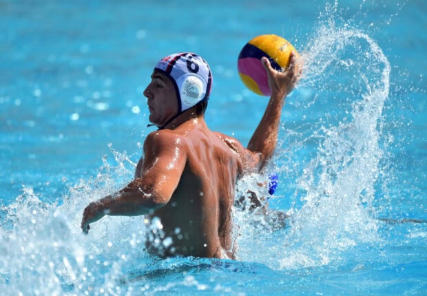 Male athlete playing water polo with ball in pool splashing water around