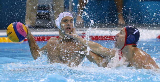 Male water polo player holding ball while being defended in a water polo match