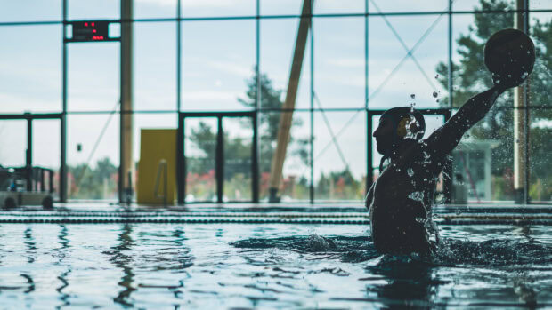 Male water polo player preparing to throw the ball in the indoor pool