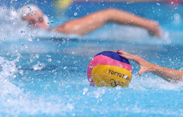 A water polo player reaching for the ball during a competitive match in a pool with splashing water