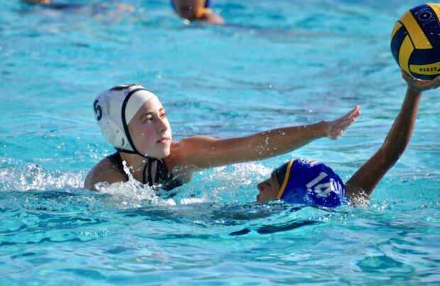 Female water polo player reaching for the ball during a competitive water polo match
