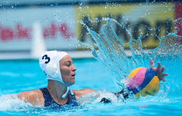 Female water polo player wearing number three cap reaching for the ball in the pool water splashing around