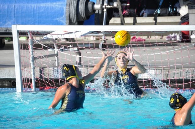 Female water polo players contesting the ball near the goal in the pool