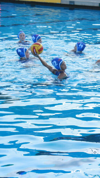 Female water polo players competing in a pool during a match with a ball in hand