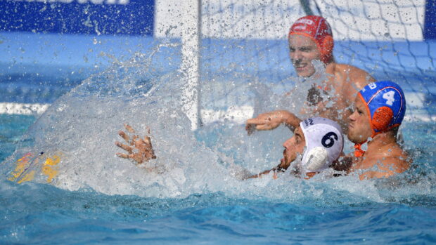 Water polo players competing intensely near the goal in a pool with splashing water