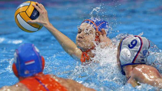 Female water polo player reaching to throw the ball during a match in the pool