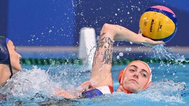 Female water polo player with tattooed arm preparing to throw water polo ball in the pool