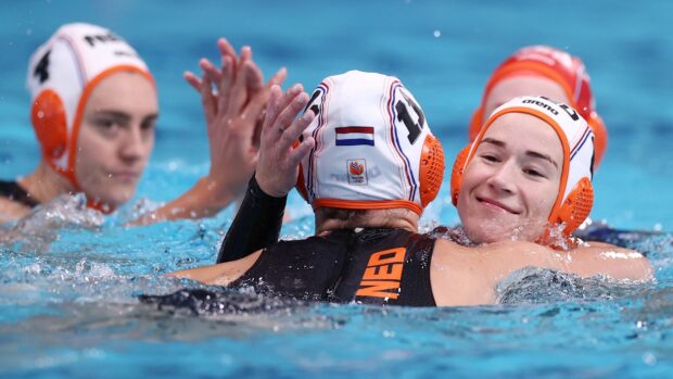 Female water polo players celebrating a win in the pool wearing caps with Netherlands flag