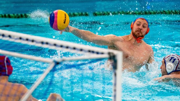 A water polo player reaching to block a colorful water polo ball during a match in a swimming pool
