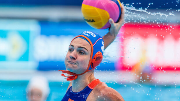 Water polo player wearing a blue cap throwing a yellow and pink ball in the pool
