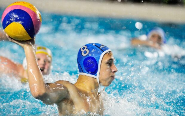 A water polo player wearing a blue cap prepares to throw the ball in the pool