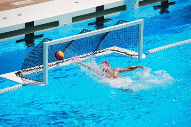 Water polo player diving to save the ball in a swimming pool goal