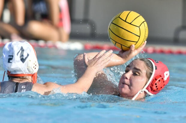 A water polo player in red cap preparing to throw the ball during a match in a swimming pool